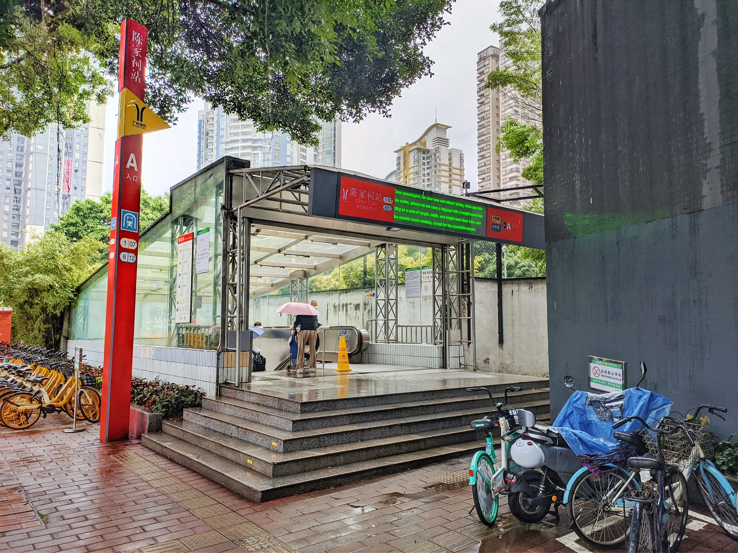 Exit A of Chen Clan Academy metro station: a red sign post, and a covered stairway down, on a rainy day