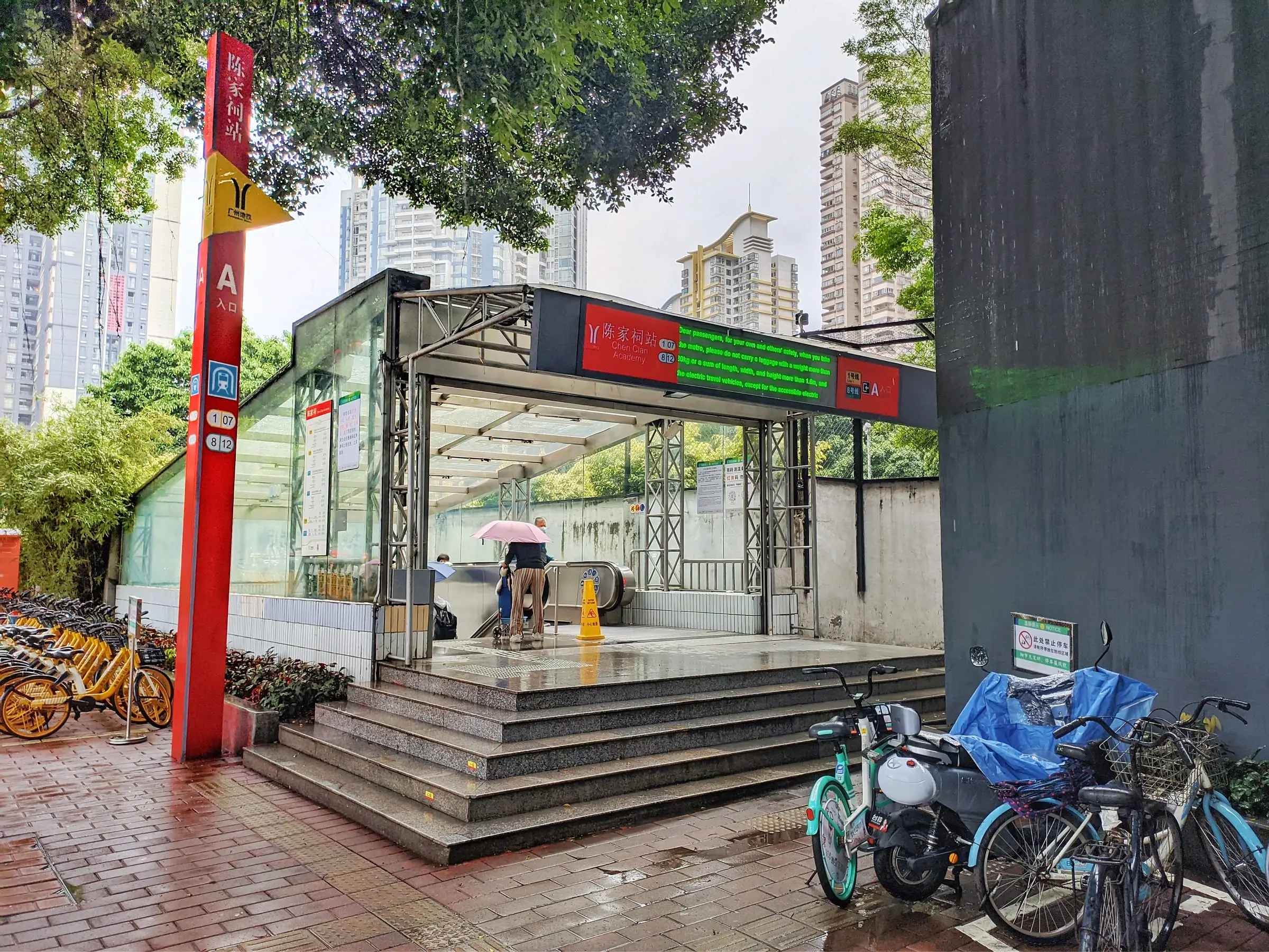 Exit A of Chen Clan Academy metro station: a red sign post, and a covered stairway down, on a rainy day